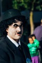 Man dressed as Charles Chaplin with his face painted white and mustache. Black hat