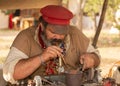 A man dressed in 1800`s period clothing as a copper smith blows on a small pan of coals to heat the piece of copper Royalty Free Stock Photo