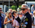 A man dressed in student uniform, baseball cap and sunglasses is taking photos while walking in the parade Lundakarnevalen 2018