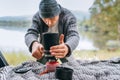 A man dressed in warm knitted clothes portrait starting a gas burner stove in the cozy car trunk with a beautiful mountain lake