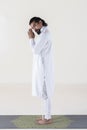 A man dressed in white on a mat, clasping hands while looking at camera over white background. .Tadasana yoga pose Royalty Free Stock Photo