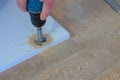 Man drill round hole for door hinges in chipboard usinf electric drill, closeup.
