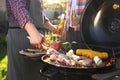 Man with drink cooking meat and vegetables on barbecue grill outdoors, closeup Royalty Free Stock Photo