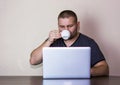 Man drinking a cup of coffee on a laptop. Young man drinks coffee