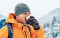 Man drinking a hot drink from thermos flask dressed bright orange softshell jacket while he trekking winter mountains route. Royalty Free Stock Photo