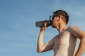 Man Drinking Water After Running. Portrait of a handsome athletic man with a naked body drinking water from a bottle against a