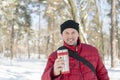 Man drinks tea out of cup. Winter forest. Young man in a red warm jacket with knitted hat and scarf standing on snowy background a Royalty Free Stock Photo