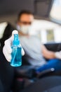 Driver with face mask and medical gloves holding disinfectant spray bottle in car, coronavirus pandemic concept