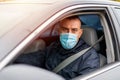 A man driving a car puts on a medical mask