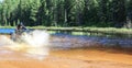 Man driving motocross ATV quad through splashing river lake water with high speed. Foy, Foyross Lake, Sudbury, Canada.