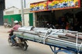 A man driving a motorcycle with an attached trailer loaded with metal pipes, Phnom Penh, Cambodia