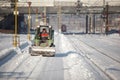 Man driving a small excavator to remove snow from the Northern Railway Station Gara de Nord during a cold, sunny and snowy day