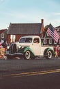 Man driving a vintage white 1939 Ford Pickup, with the American flag, and people on the street Royalty Free Stock Photo