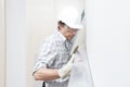 Man drywall worker or plasterer checking level of white plasterboard wall with bubble level at construction site. Wearing white Royalty Free Stock Photo