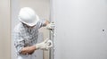 Man drywall worker or plasterer putting mesh tape for plasterboard on a wall using a spatula and plaster. Wearing white hardhat,