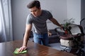 man dusting table with rag and holding pram with other hand