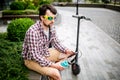 Man with e-scooter relaxing and using smartphone on bench in city. Modern male with electro scooter sitting on bench in park while Royalty Free Stock Photo