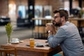 Man with earphones enjoying cup of coffee at cafeteria, sitting alone at table