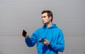 Man with earring holds two smartphones in both hands, look at them with serious face, wearing in blue hoody, black fitness tracker