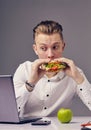 Man eat hamburger in office while watch video on his laptop Royalty Free Stock Photo