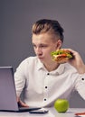Man eat hamburger in office while watch video on his laptop Royalty Free Stock Photo