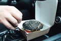 Man is eating black burger with meat, fish, tomato, salad, sause in car. Fast, safe, takeaway food on the road to coronavirus Royalty Free Stock Photo