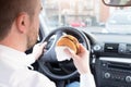 Man eating junk food and driving seated in car Royalty Free Stock Photo