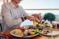 Man eats fish with vegetables in outdoors restaurant. Fresh seafood dinner with sea landscape. Summer vacation Royalty Free Stock Photo