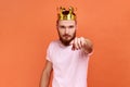 Man egoistically looking at camera posing with crown on head pointing at you with serious expression