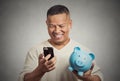 Man employee holding piggy bank looking at smart phone