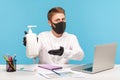 Man employee in hygienic mask pointing bottle with antiseptic gel, recommending disinfection to prevent coronavirus Royalty Free Stock Photo