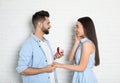 Man with engagement ring making marriage proposal to girlfriend near brick wall