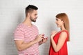 Man with engagement ring making marriage proposal to girlfriend near brick wall