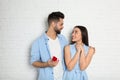 Man with engagement ring making marriage proposal to girlfriend near brick wall