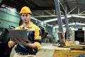 Man engineer wear yellow hard hat and wearing safety uniform standing at forklift using laptop working at heavy industrial factory