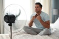 Man enjoying air flow from fan on bed in room. Summer heat Royalty Free Stock Photo