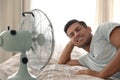 Man enjoying air flow from fan on bed in room. Summer heat Royalty Free Stock Photo