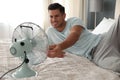 Man enjoying air flow from fan on bed in room. Summer heat Royalty Free Stock Photo