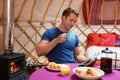 Man Enjoying Breakfast Whilst Camping In Traditional Yurt