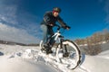 Man enjoys his ride on a bicycle in a deep snow, next to the riv Royalty Free Stock Photo