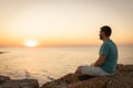 A man enjoys the view of the sunset on the sea, sitting on a rock. Royalty Free Stock Photo