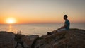 A man enjoys the view of the sunset on the sea, sitting on a rock. Royalty Free Stock Photo