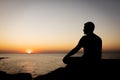 A man enjoys the view of the sunset on the sea, sitting on a rock. Royalty Free Stock Photo