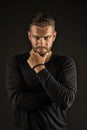 Man with evil look isolated on dark background. Macho touching his beard. Man in black jumper wearing beaded bracelet