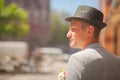 A man expects a woman on a date. The guy in the boho hat looks toward the street