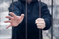 Man extends his hand for help from cage. Closeup on hands of man sitting in jail, prisoner concept. Hope to be free