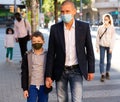 Man in face mask walking with preteen son along city street