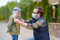 Man in facemask putting face shield on child on street or park. Safety during COVID-19 outbreak. Lifting virus lockdown. Social