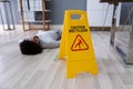 Man Falling On Wet Floor In Front Of Caution Sign Royalty Free Stock Photo