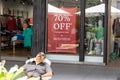 Man falls asleep in outdoor chair in front shop window and discount sign waiting for shopping wife